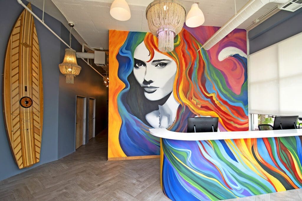 Modern med spa lobby with a colorful rainbow mural, white reception desk, and a wooden surfboard on a blue wall.
