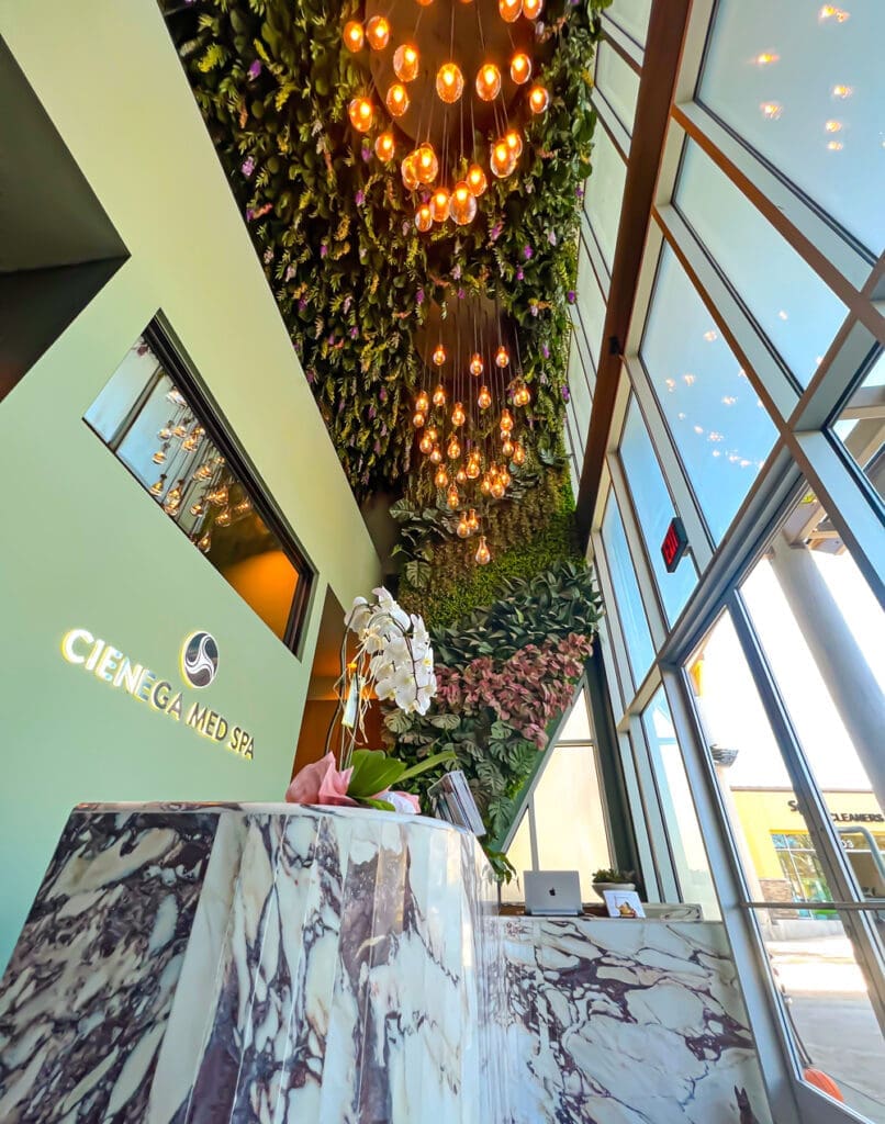 Modern medical spa lobby with marble desk, green plant ceiling, and sage green walls.